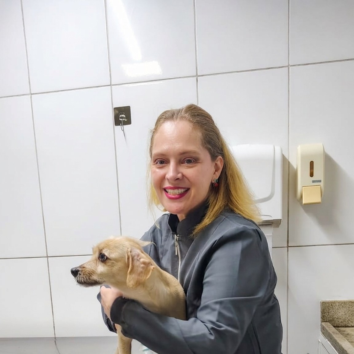 Veterinária sorrindo segurando cãozinho na mesa de atendimento da Clínica Veterinária Alfa